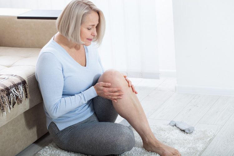 Middle-aged woman suffering from pain in leg at home, closeup. Physical injury concept.